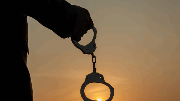 Silhouette of a hand holding handcuffs against a sunset.