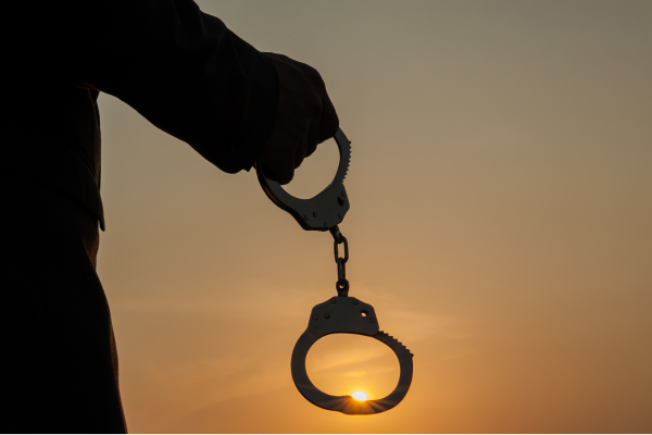 Silhouette of a hand holding handcuffs against a sunset.