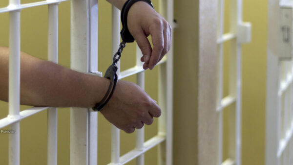 a pair of hands through prison bars with handcuffs