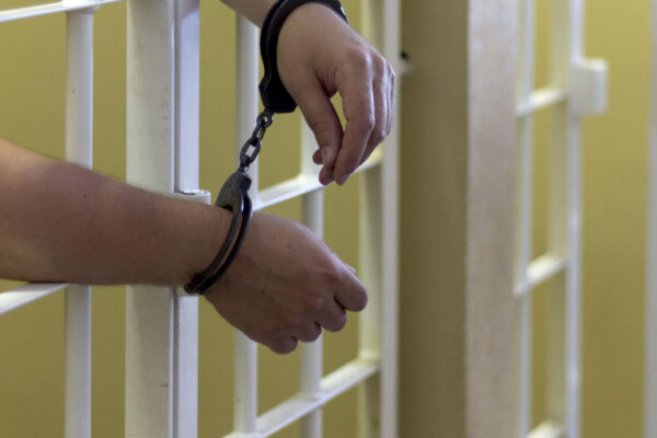 a pair of hands through prison bars with handcuffs