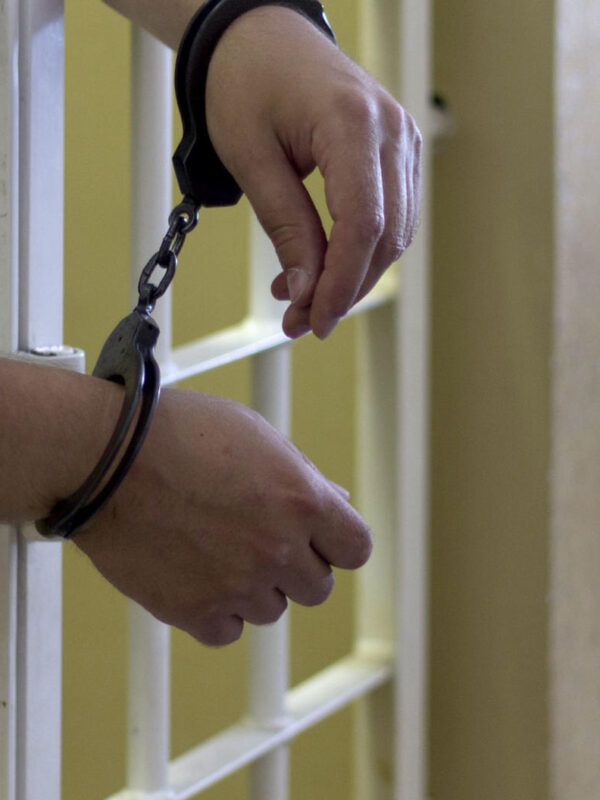 a pair of hands through prison bars with handcuffs