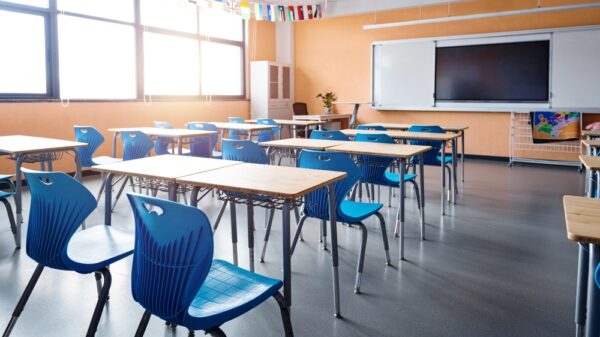 Empty school classroom with chairs and desks, a tv on the whiteboard, and orange walls