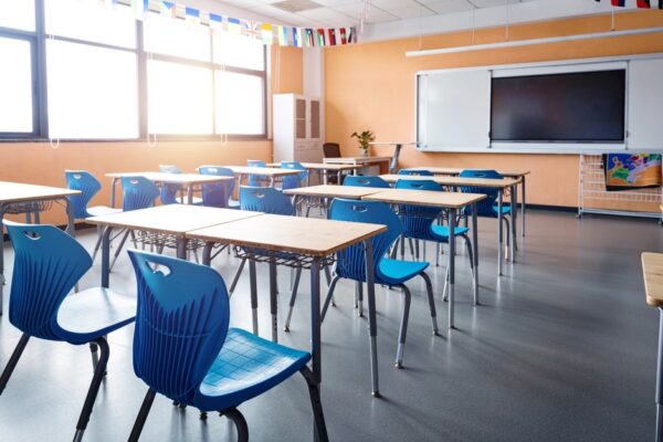 Empty school classroom with chairs and desks, a tv on the whiteboard, and orange walls