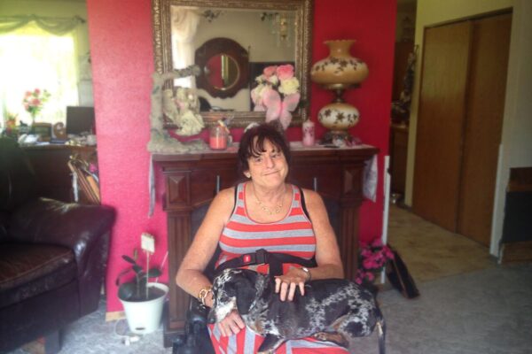 Lawsuit plaintiff Christie Mathwig sitting in a wheel chair with her dog on her lap in her house