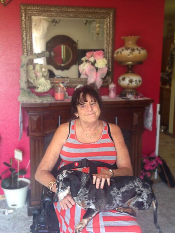 Lawsuit plaintiff Christie Mathwig sitting in a wheel chair with her dog on her lap in her house