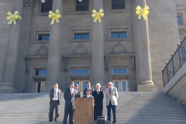 Podium on Idaho state capitol steps with people standing behind speaker at podium