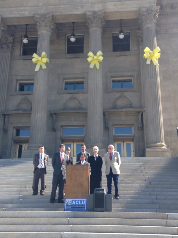 Podium on Idaho state capitol steps with people standing behind speaker at podium