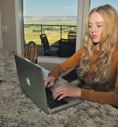 Plaintiff Sierra Norman sitting at a countertop looking at a laptop in a room with windows looking out to what looks like farmland