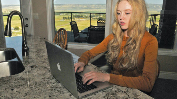 Plaintiff Sierra Norman sitting at a countertop looking at a laptop in a room with windows looking out to what looks like farmland