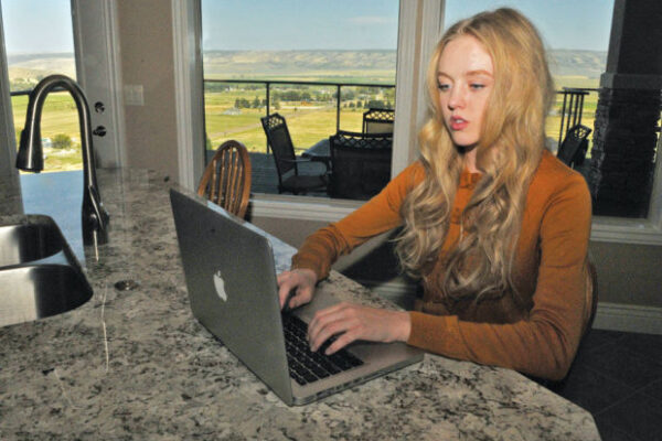 Plaintiff Sierra Norman sitting at a countertop looking at a laptop in a room with windows looking out to what looks like farmland