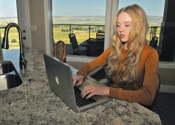 Plaintiff Sierra Norman sitting at a countertop looking at a laptop in a room with windows looking out to what looks like farmland