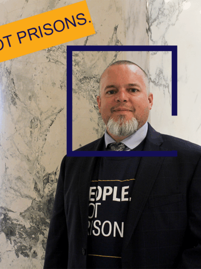 Jason is a tanned middle aged man with a salt and pepper beard, looking pleasantly at the camera from inside the marble rotunda in the Idaho State Capitol Building.