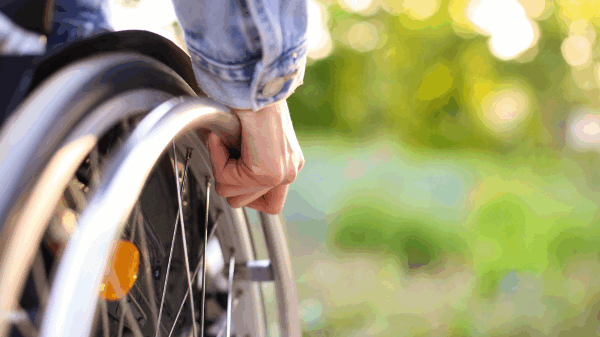 Close-up of a person's hand on the wheel of their wheelchair, with greenery in the background