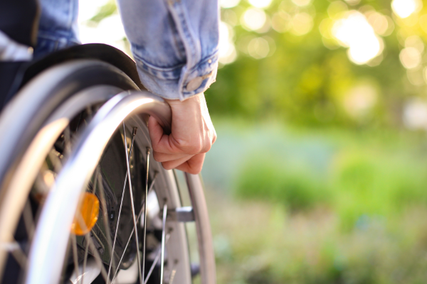 Close-up of a person's hand on the wheel of their wheelchair, with greenery in the background