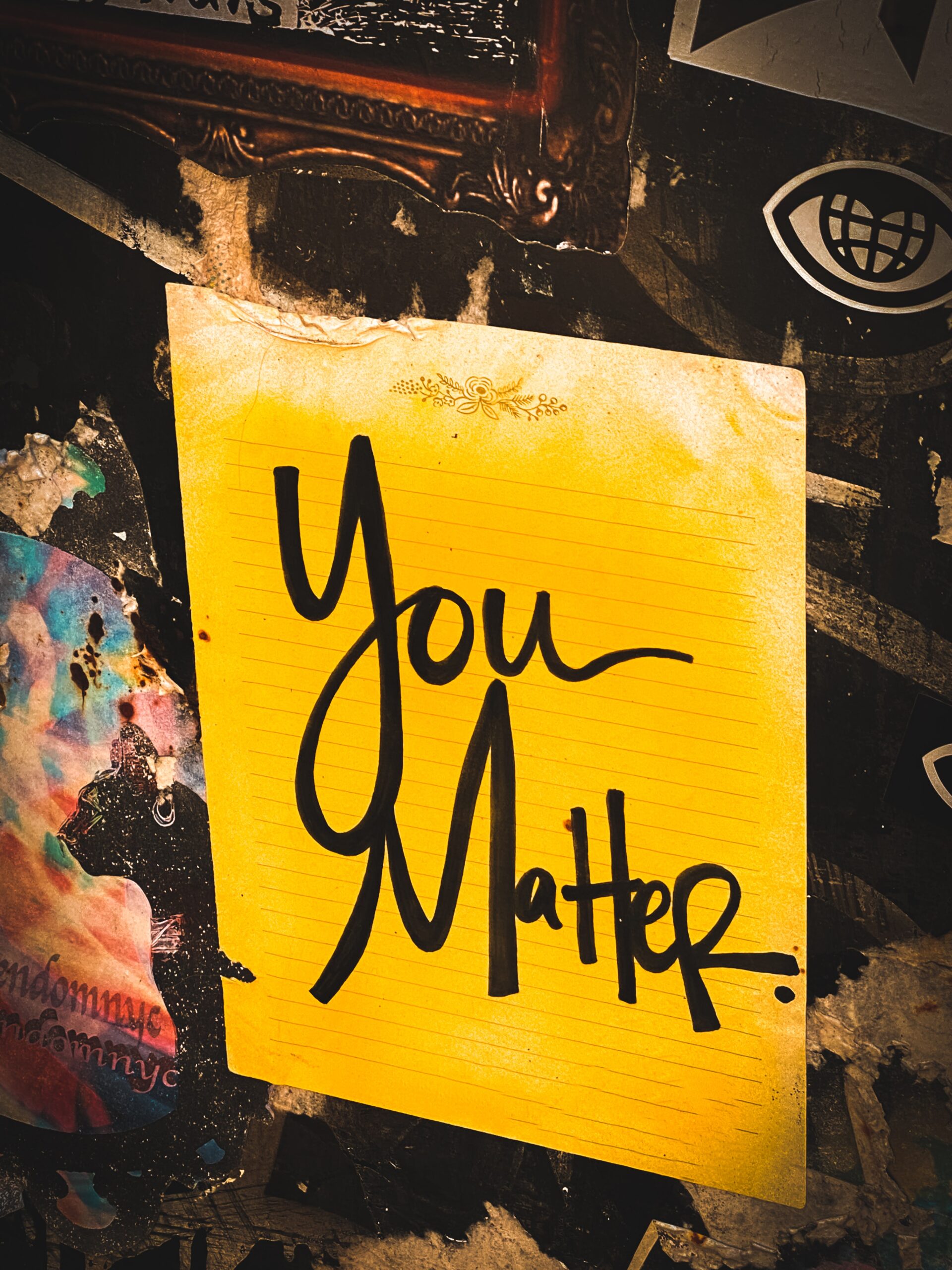 A yellow piece of paper is on a dark wall. The words on the paper say "You Matter" in black letters.