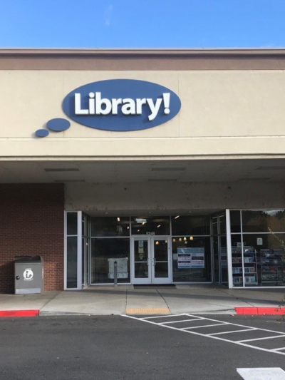 A picture of the Hillcrest Library in Boise. A light brown building with a blue circular sign that says "Library!"