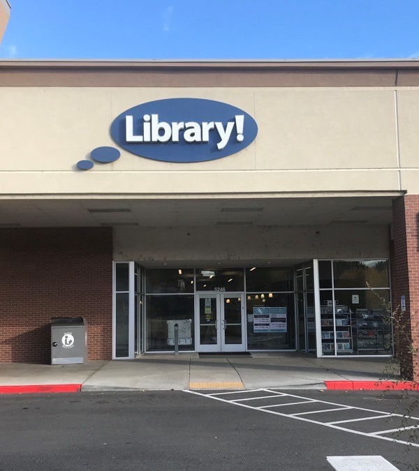 A picture of the Hillcrest Library in Boise. A light brown building with a blue circular sign that says "Library!"