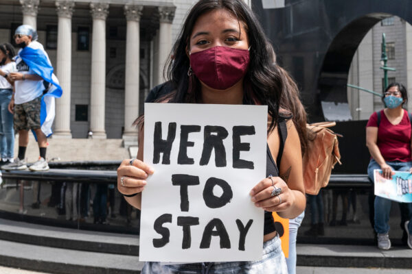 Young girl holding a sign that says "here to stay"