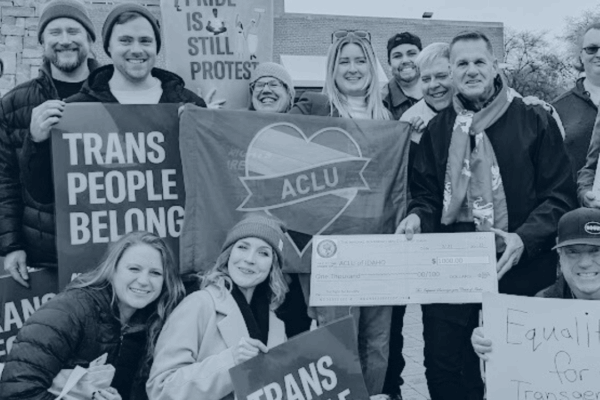 Blue tinted picture of ACLU staff holding signs that say Trans People Belong and Pride is Still Protest