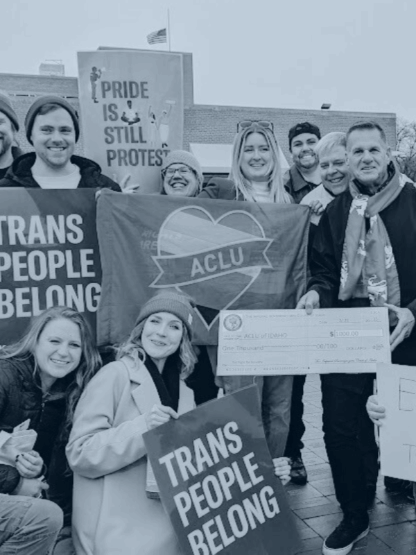 Blue tinted picture of ACLU staff holding signs that say Trans People Belong and Pride is Still Protest
