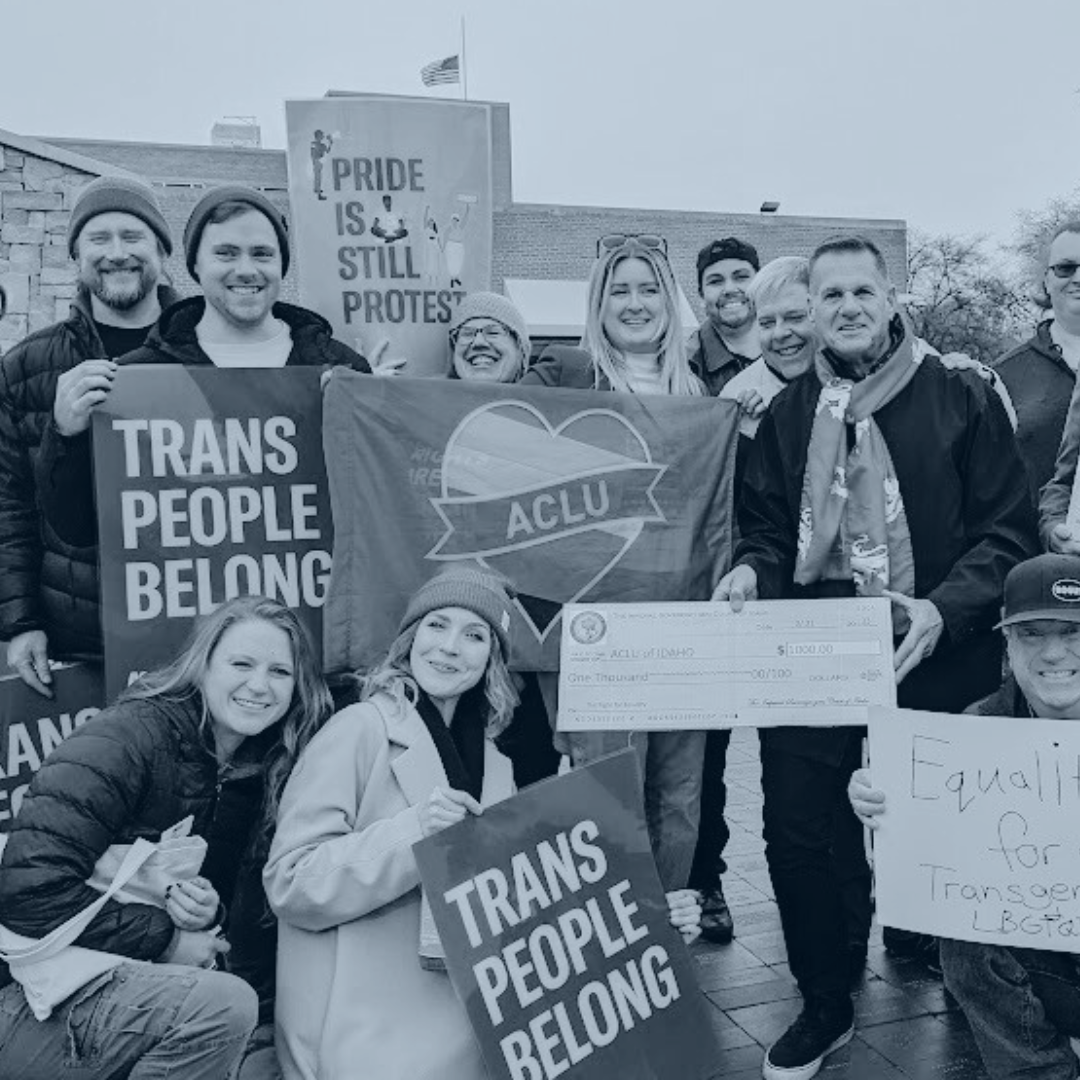 Blue tinted picture of ACLU staff holding signs that say Trans People Belong and Pride is Still Protest