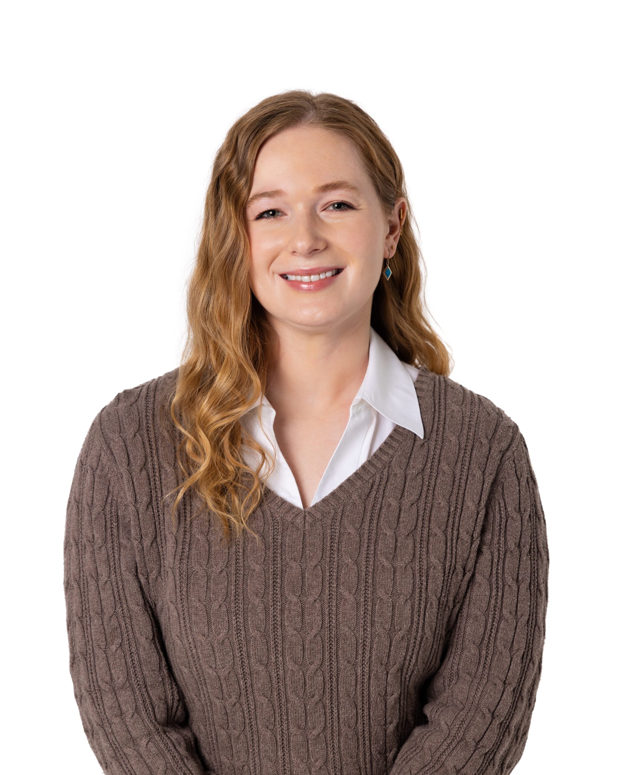 Taylor Munson is a white woman with red hair just past her shoulders. She is wearing a white collared shirt with a brown sweater over it.