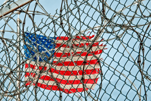 A worn American flag is covered by barb wire outside a prison