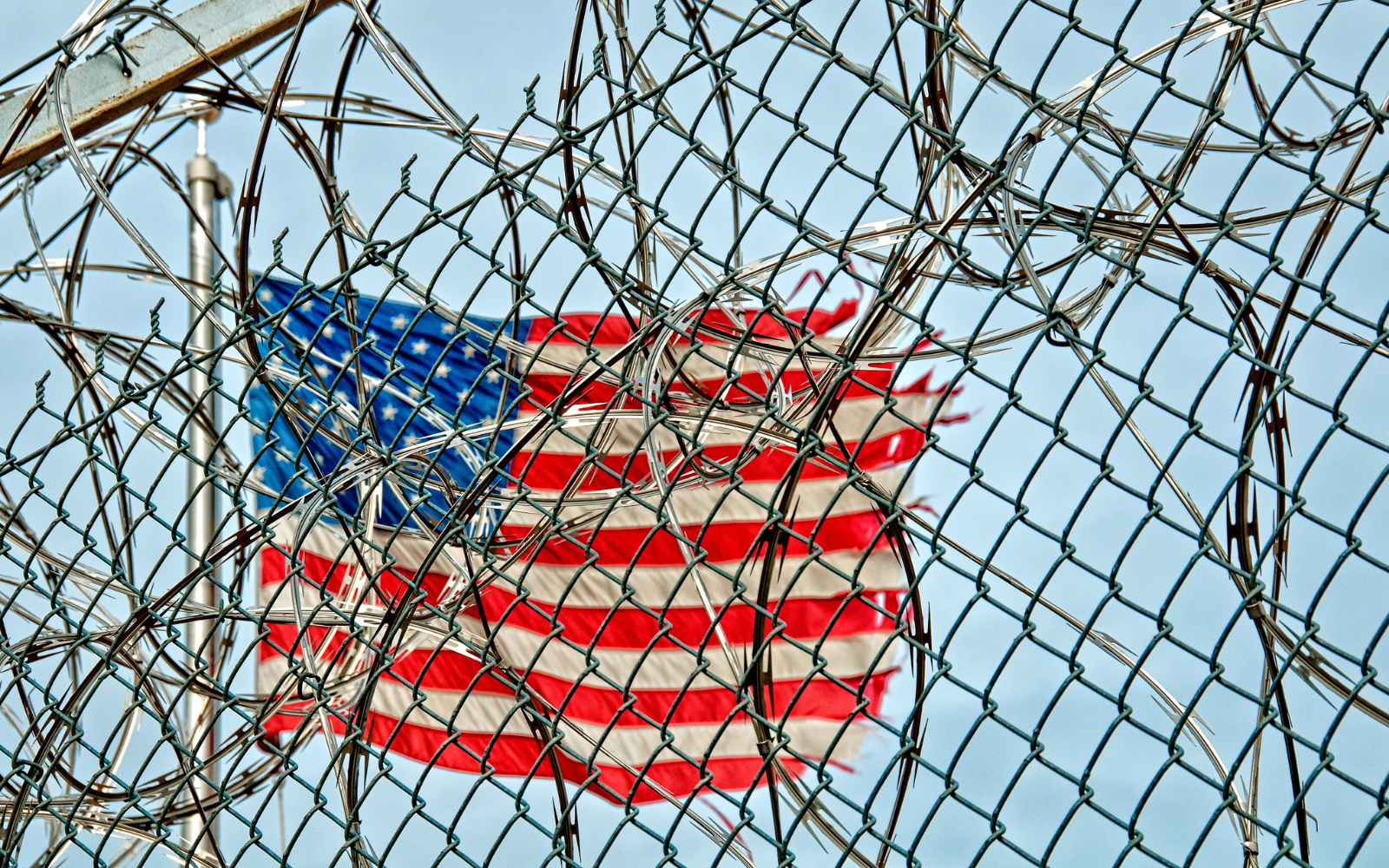 A worn American flag is covered by barb wire outside a prison