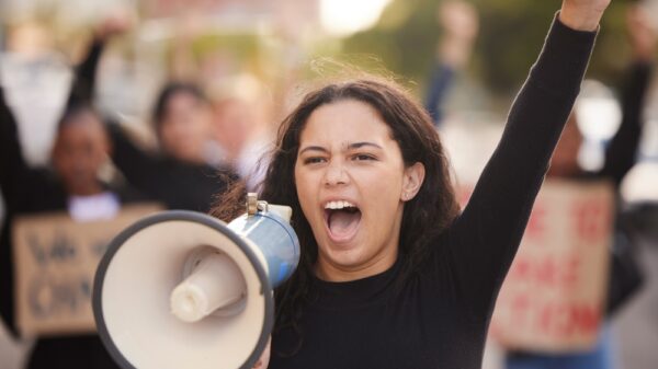 A person holding a megaphone with a raised fist at a protest rally.