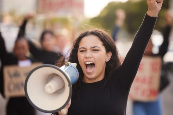 A person holding a megaphone with a raised fist at a protest rally.