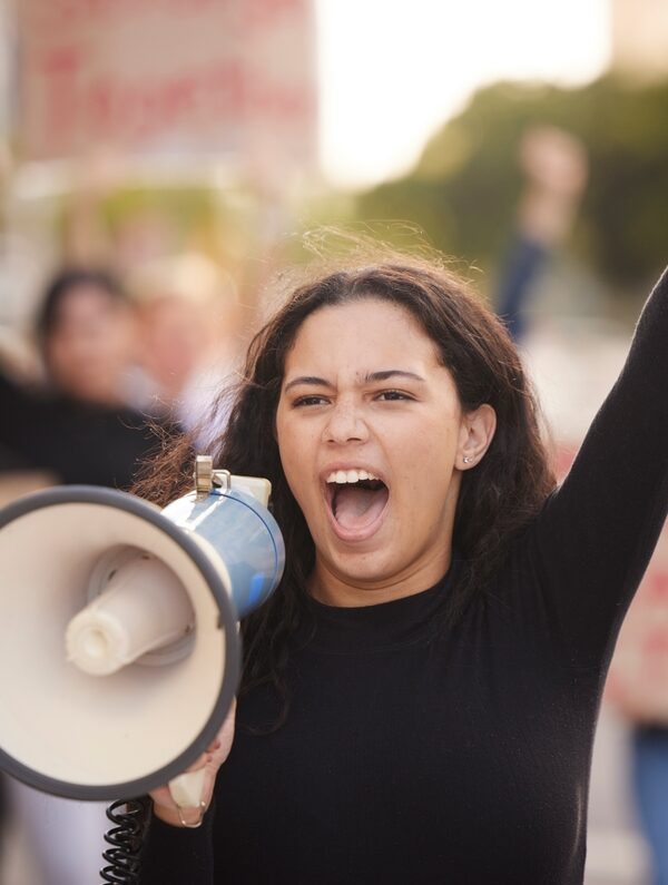 A person holding a megaphone with a raised fist at a protest rally.