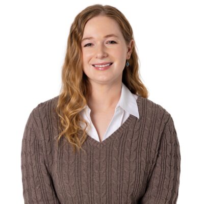 White woman with red hair wearing a brown sweater.