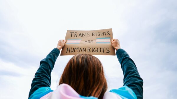 Person wearing a trans flag holding a sign up that says 'trans rights are human rights'