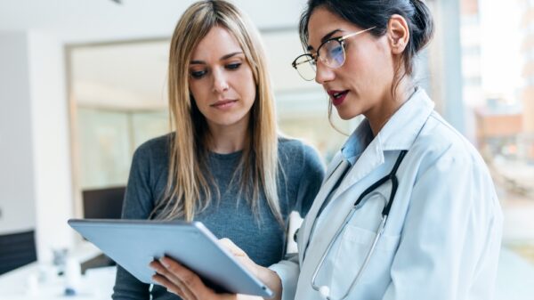 Female doctor is explaining something to a female patient while looking at a clipboard.