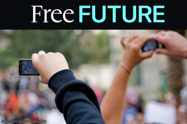 Hands in the air holding cellphones with a protest in background