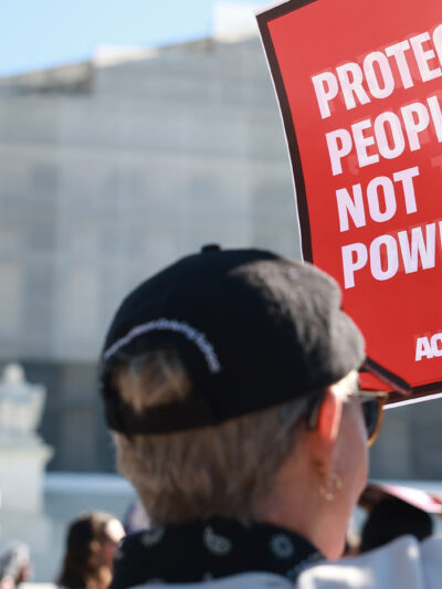 An individual holding a sign that says "Protect People, Not Power" outside of the U.S. Supreme Court ahead of arguments in the Voting Rights case Callais v. Landry.