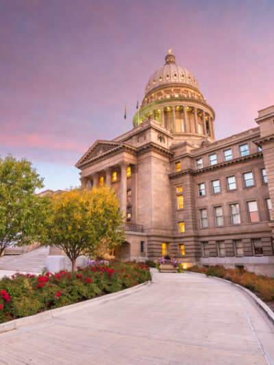 View of the Idaho Capitol on the right side looking up with blooming flowers and a pink sky