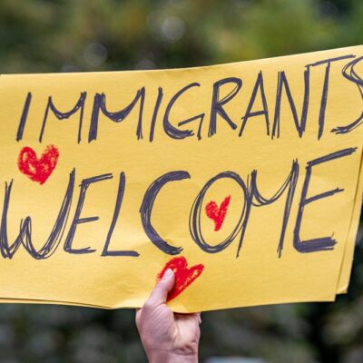 Person holding yellow sign with hearts that reads "immigrants welcome"