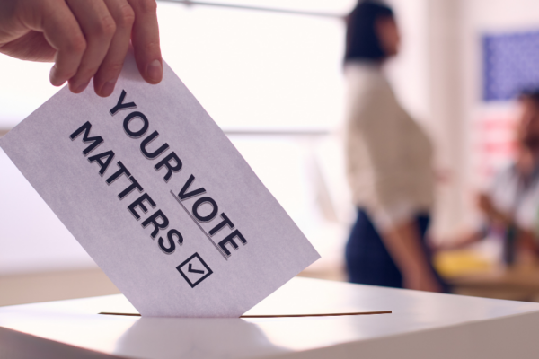 A hand putting a piece of paper in a ballot box with the words "your vote matters"