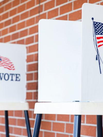 Three ballot boxes sit in front of a brick wall with "vote" on the outside
