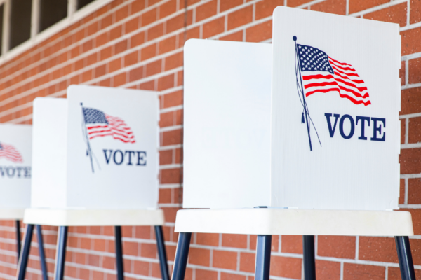 Three ballot boxes sit in front of a brick wall with "vote" on the outside