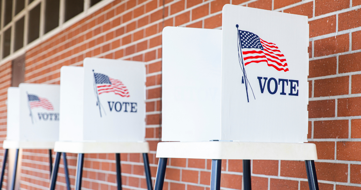 Three ballot boxes sit in front of a brick wall with "vote" on the outside