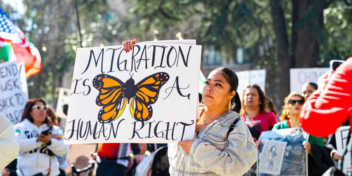 A woman is attending an immigrant rights protest and holds a signs with an image of a butterfly that says "migration is a human right"