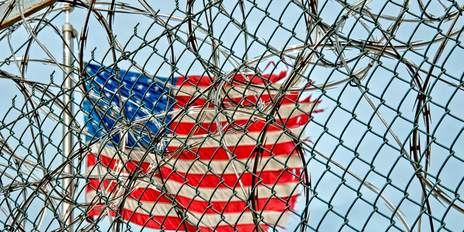 A worn American flag is covered by barb wire outside a prison