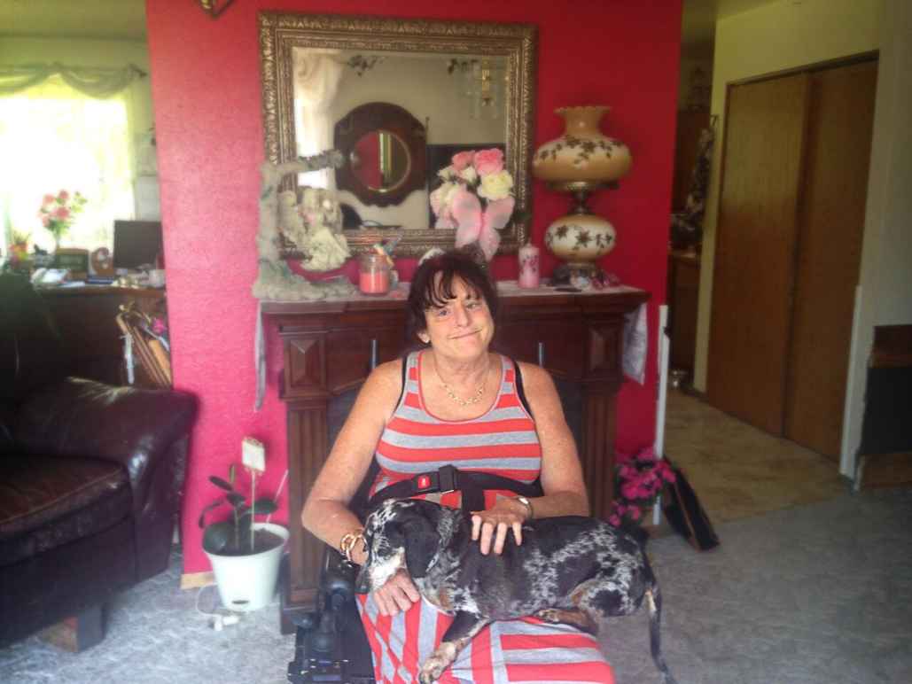 Lawsuit plaintiff Christie Mathwig sitting in a wheel chair with her dog on her lap in her house 