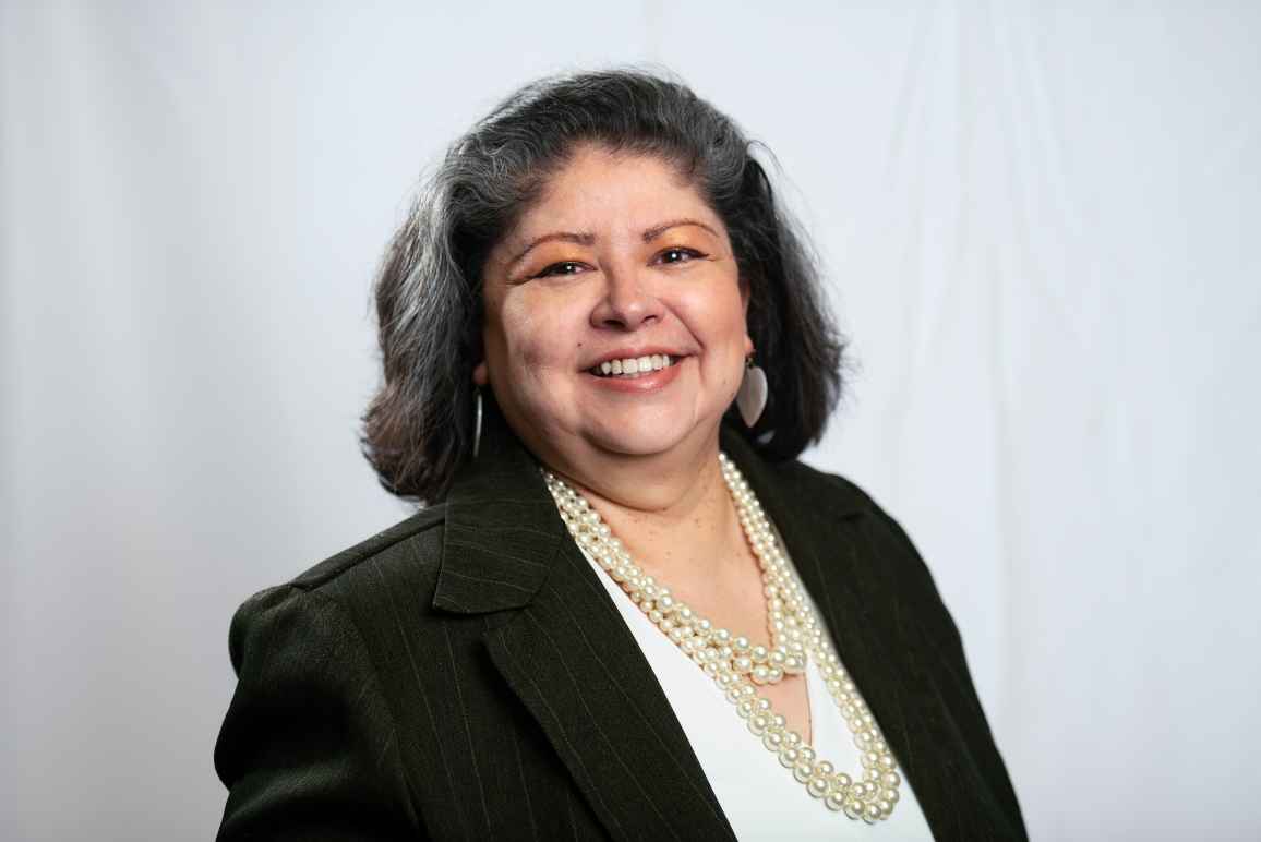 Dina is centered in front of a white cloth background.