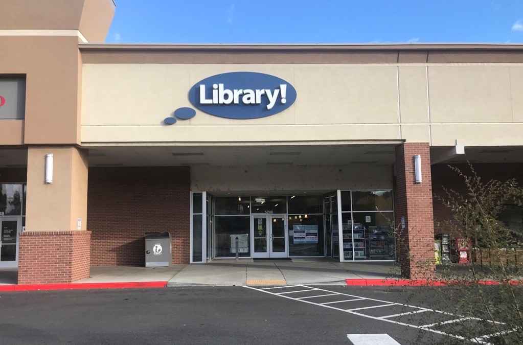 A picture of the Hillcrest Library in Boise. A light brown building with a blue circular sign that says "Library!"