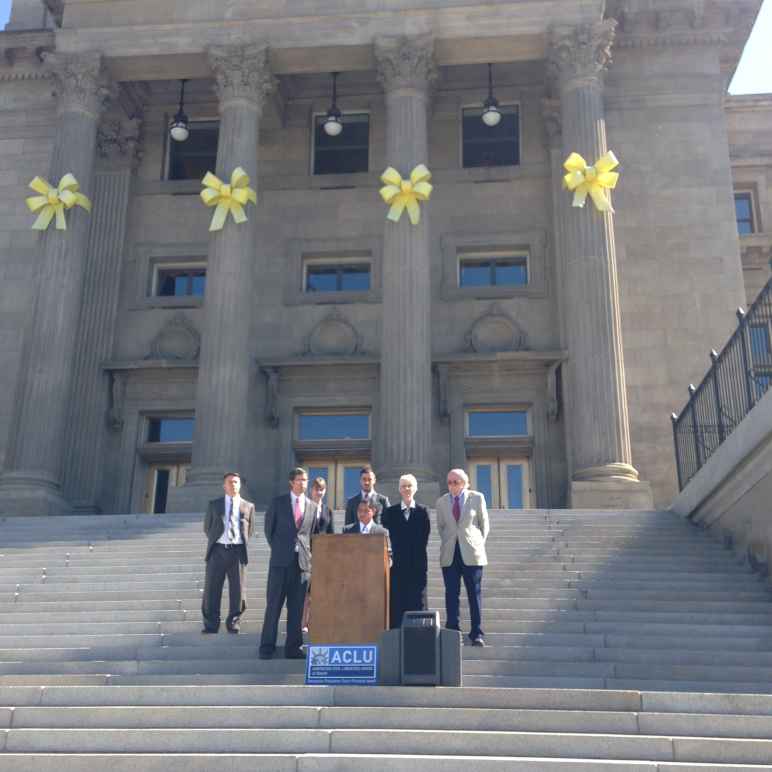 Podium on Idaho state capitol steps with people standing behind speaker at podium