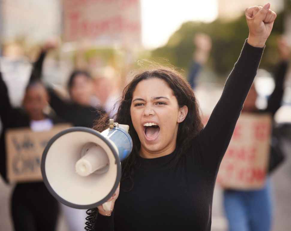 A person holding a megaphone with a raised fist at a protest rally.