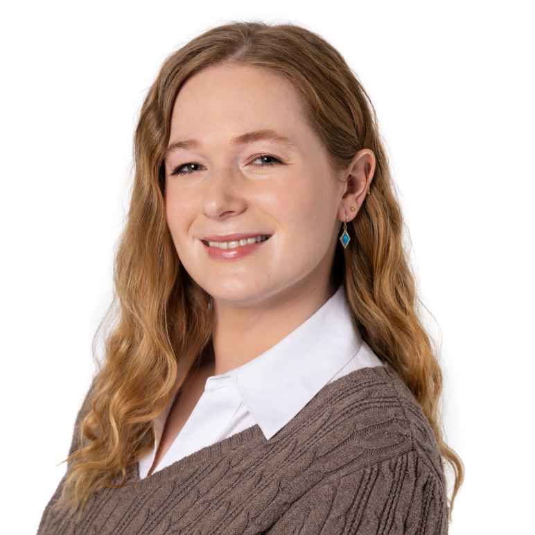 Taylor Munson is a white woman with red hair just past her shoulders. She is wearing a white collared shirt with a brown sweater over it. 